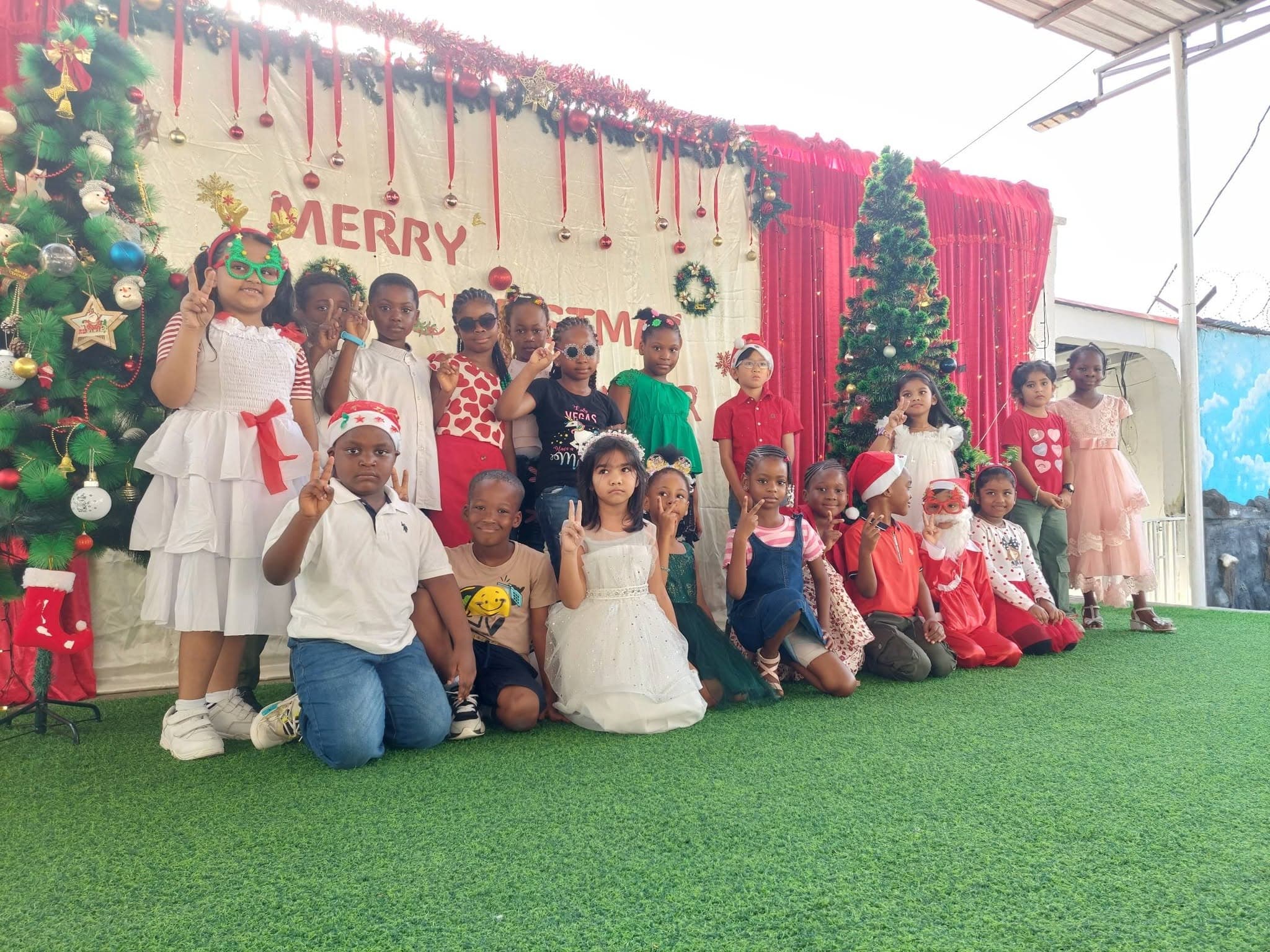 Young students dressed up in front of the Merry Christmas backdrop