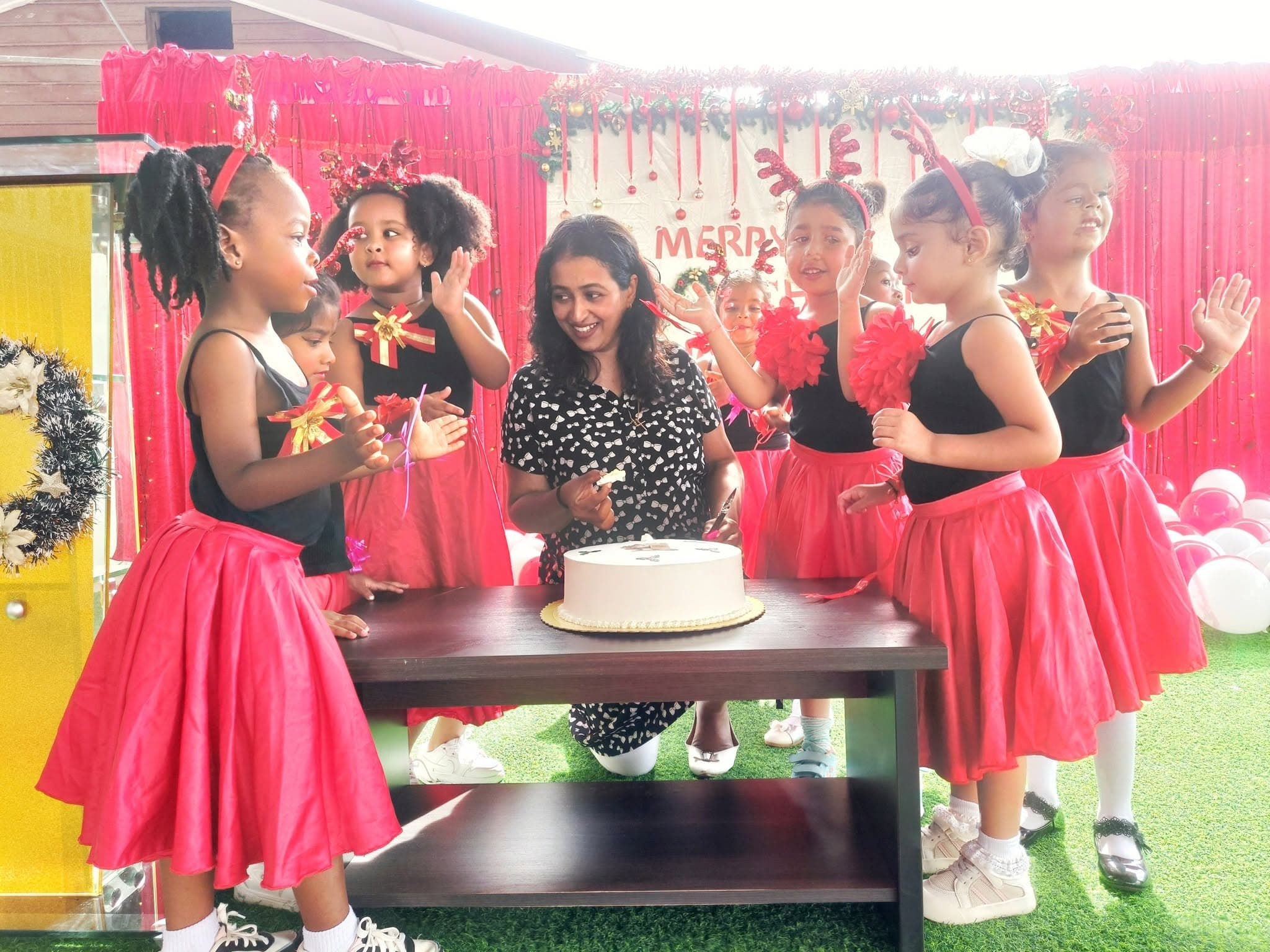 Nursery dancers in red skirts cutting the Christmas cake with a teacher