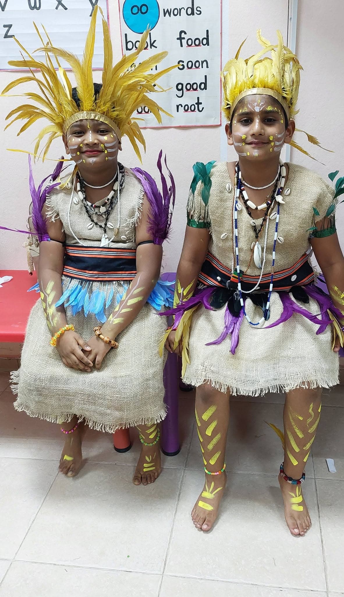 Two students smiling in feathered headdresses and traditional face paint